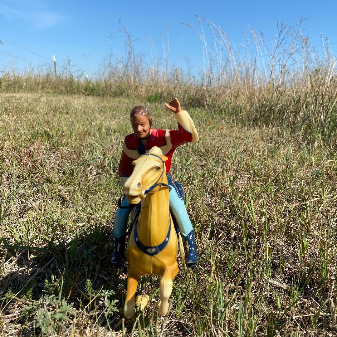 little plastic cowboy riding a little plastic horse in a meadow